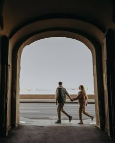 a man and woman holding hands as they walk through an archway