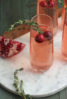 three glasses filled with pink wine and garnish on a marble platter next to pomegranates