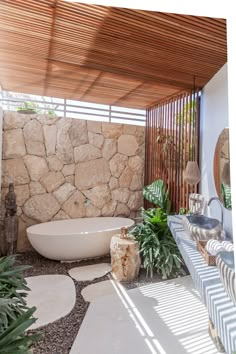 an outdoor bathroom with stone walls and a large bathtub in the center, surrounded by greenery