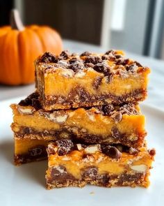 three pieces of chocolate chip cookie bars stacked on top of each other, with a pumpkin in the background