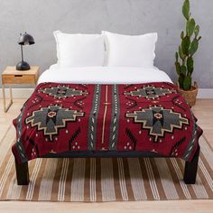 a bed with a red blanket on top of it next to a potted plant