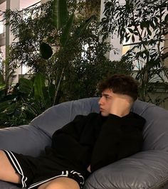 a young man sitting on top of a blue couch next to a potted plant