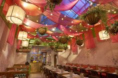 the interior of a restaurant with many tables and hanging plants on the ceiling above them