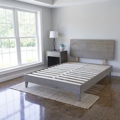 a bed sitting on top of a hard wood floor next to a window with white curtains