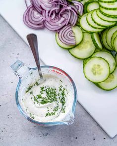 cucumbers and onions on a cutting board next to a bowl of ranch dressing