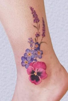 a flower tattoo on the foot of a woman's leg with purple and blue flowers