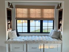 a window seat with pillows on it in front of a window and bookshelves