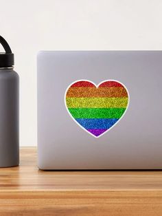 a rainbow heart sticker on the back of a macbook pro with a water bottle next to it