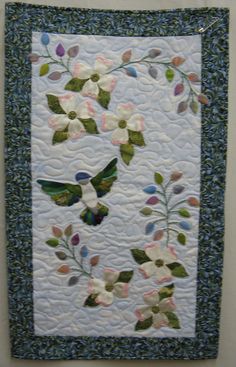 a close up of a quilted wall hanging with flowers and leaves on the border