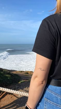 a woman with a tattoo on her arm looking at the ocean