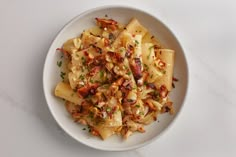 a white bowl filled with pasta covered in sauce and toppings on top of a table