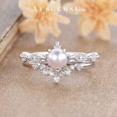 a white pearl and diamond ring sitting on top of a wooden table next to flowers