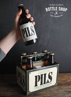 a person holding a bottle in front of a box of pils on a table