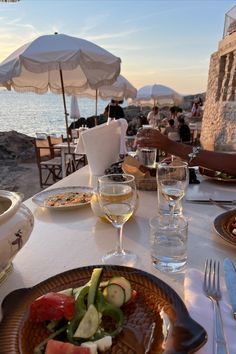 an outdoor dining area with plates of food and wine glasses on the table, overlooking the ocean