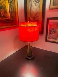 a red lamp sitting on top of a wooden table next to pictures and framed art