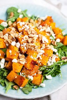 a salad with nuts and spinach leaves on a blue plate sitting on a white table cloth