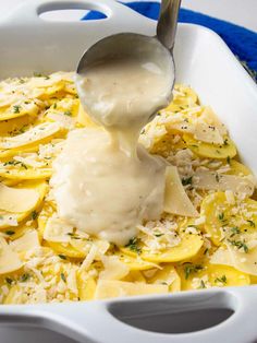 a spoon is pouring sauce over some ravioli in a white casserole dish