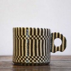 a black and white striped coffee cup sitting on top of a wooden table next to a wall