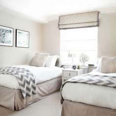 two beds in a bedroom with white walls and carpeted flooring next to windows