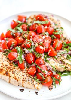 a white plate topped with chicken, tomatoes and green garnish on top of it