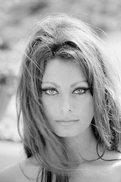 a woman with long hair and blue eyes posing for a black and white photo on the beach