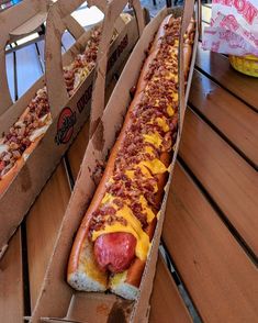 two hotdogs with toppings sit in cardboard boxes on a table