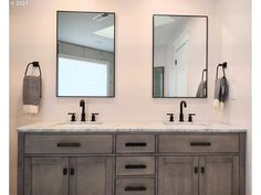 two mirrors are above the double sink vanity in this bathroom with marble countertops and gray cabinets