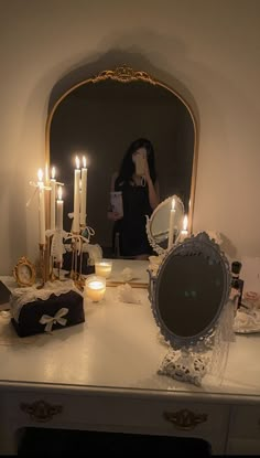 a vanity with candles, mirror and other items on it in front of a woman's reflection