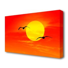 two birds flying in front of an orange and yellow sunset canvas wall art print on the wall