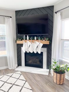 a living room decorated for christmas with stockings hanging from the mantel and potted plants