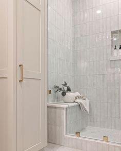 a bathroom with white tile and gold trimmings on the shower door, sink and mirror