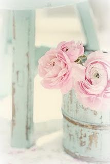 some pink flowers are in a tin can on a table with a chair behind it