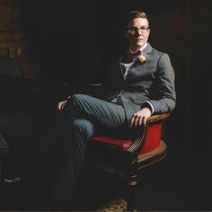 a man in a suit and tie sitting on a chair with his legs crossed, looking at the camera