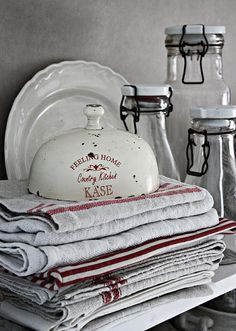 a stack of folded towels sitting on top of a white shelf next to glass jars