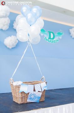 a basket with some balloons attached to it on a table in front of a blue wall