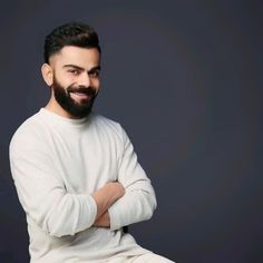 a man with a beard and white sweater sitting on a chair in front of a dark background