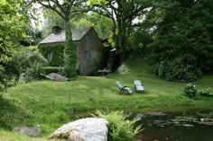 an old stone house sits next to a pond in the middle of a lush green field