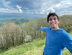 a young man standing on top of a lush green hillside