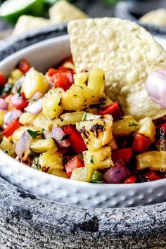 a hand dipping a tortilla chip into a bowl filled with pineapple salsa