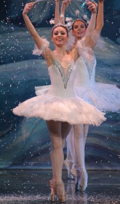 two ballerinas in tutu and leotards with their arms raised above their heads