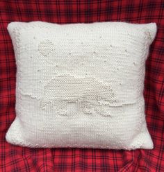 a white knitted pillow sitting on top of a red plaid bed spread with an embroidered sheep design