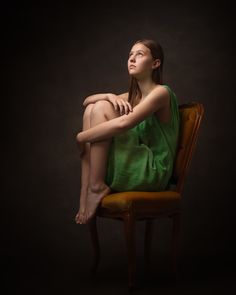 a woman in a green dress sitting on a chair with her legs crossed and looking up