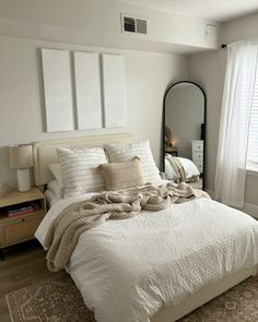 a bedroom with a bed, mirror and two lamps on either side of the window