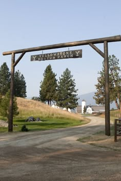 a wooden sign hanging from the side of a road next to a lush green field