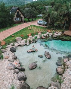 a person sitting in the middle of a pool surrounded by rocks and grass with a car parked on the other side