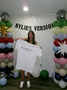 a woman holding up a t - shirt in front of balloons and streamers that read, kylie's version