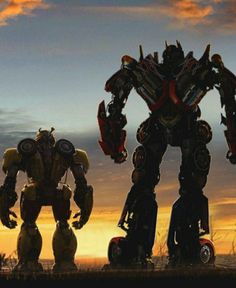 two large robots standing next to each other in front of a sunset with the sun setting behind them