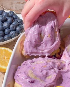 a person dipping blueberries into a bowl with lemons and blueberries in the background