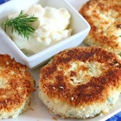 three crab cakes on a white plate with a small bowl of mashed potatoes