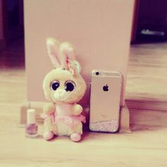 a small stuffed animal next to an iphone on a wooden floor with a pink wall in the background